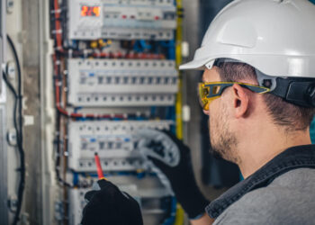 Man, an electrical technician working in a switchboard with fuses. Installation and connection of electrical equipment.